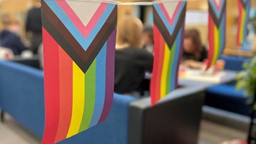 prideflaggor i förgrunden, studenter i en soffa i bakgrunden. 
