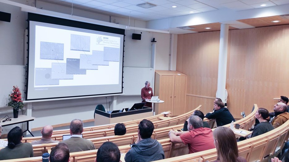 A group of people sitting in a lecture hall and following a presentation by a female scientist