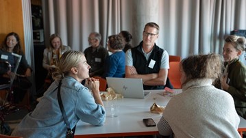 Personer sitter runt ett bord och diskuterar.
