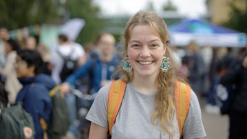 Glad blond tjej med stora örhängen som står bland massa folk.