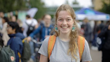 A cheerful blonde girl with large earrings standing in the middle of a crowd.