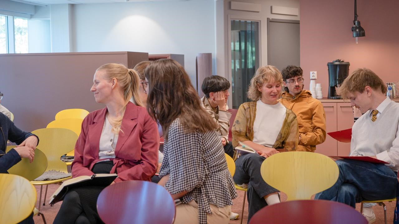 En grupp människor som sitter på stolar i ett rum och pratar.