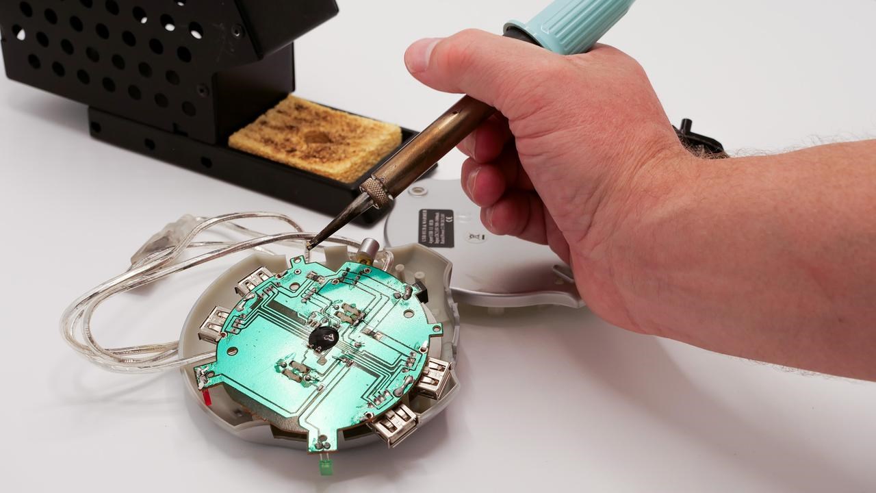 En person använder ett lödverktyg på en elektronisk utrustning.