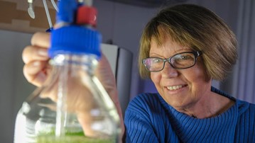 A researcher in a lab with her hand stretched out towards a lab bottle.