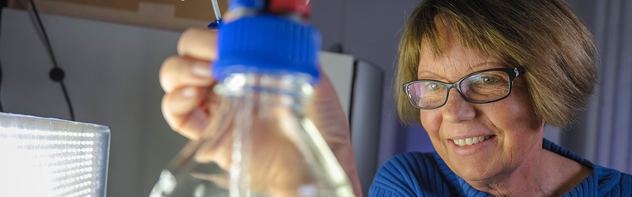 A researcher in a lab with her hand stretched out towards a lab bottle.