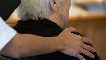Detalj - hand på äldre kvinnas rygg på äldreboende.