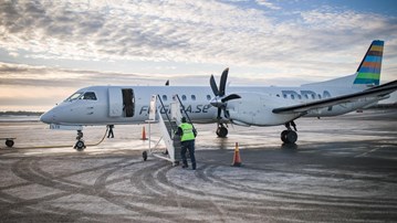 Ett flygplan som står på landningsplattan på Umeå flygplats. En flygplatsanställd håller på att ansluta trappan för att passagerare ska kunna gå ur planet.