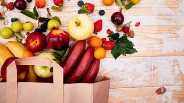Frukt och bär hällda ur en papperspåse på ett bord. Nyttiga livsmedel.