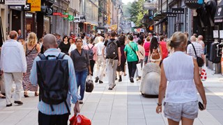 Sommardag på gågatan Drottninggatan mellan Mäster Samuelsgatan och Kungsgatan i Stockholm, Sverige, med folk i rörelse.