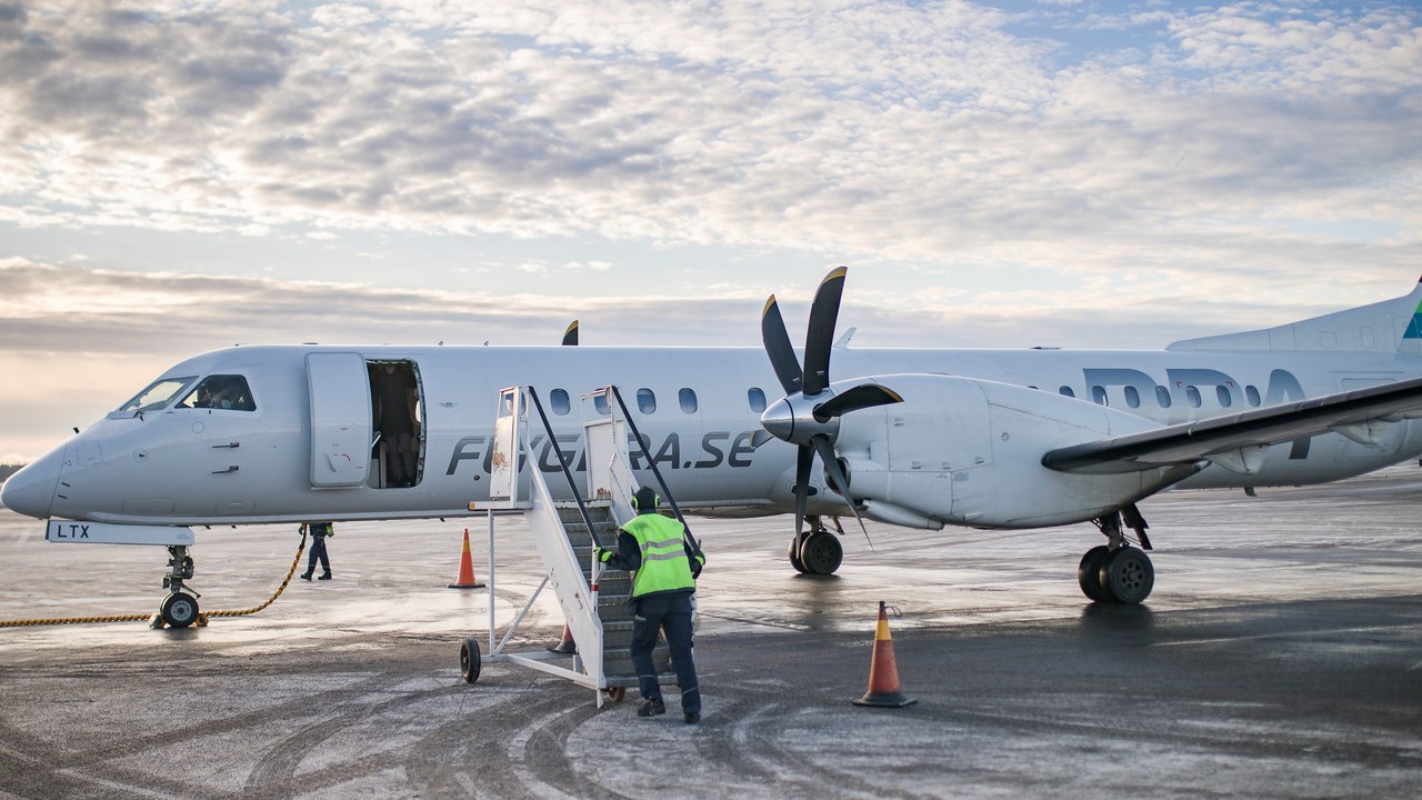 Ett flygplan som står på landningsplattan på Umeå flygplats. En flygplatsanställd håller på att ansluta trappan för att passagerare ska kunna gå ur planet.
