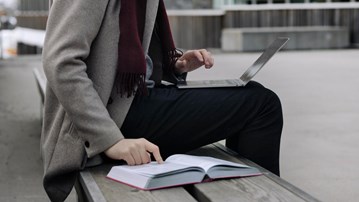 En student sitter med en bok och sin laptop och studerar.