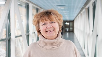 Professor Nina Khairova i en ljus korridor, iklädd en beige tröja. Hennes hår är blont och kort och hon ler. 