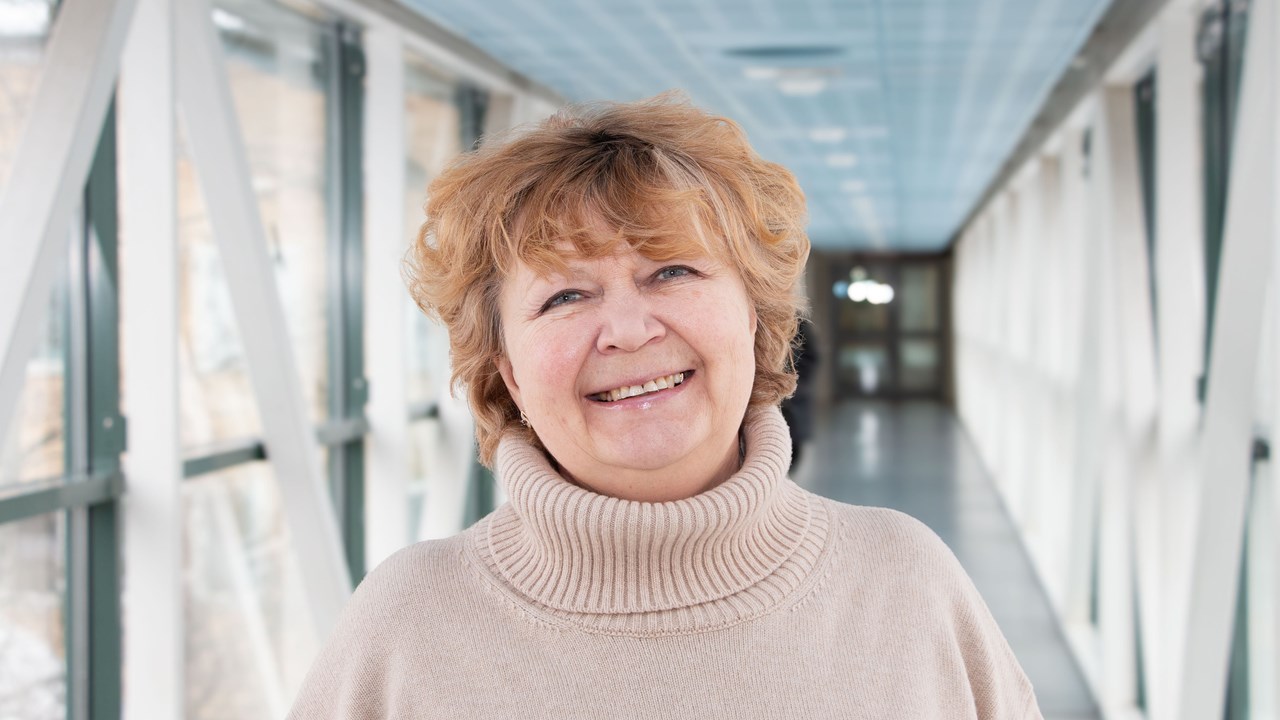 Professor Nina Khairova i en ljus korridor, iklädd en beige tröja. Hennes hår är blont och kort och hon ler.