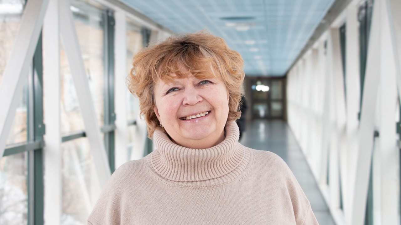 Professor Nina Khairova i en ljus korridor, iklädd en beige tröja. Hennes hår är blont och kort och hon ler.