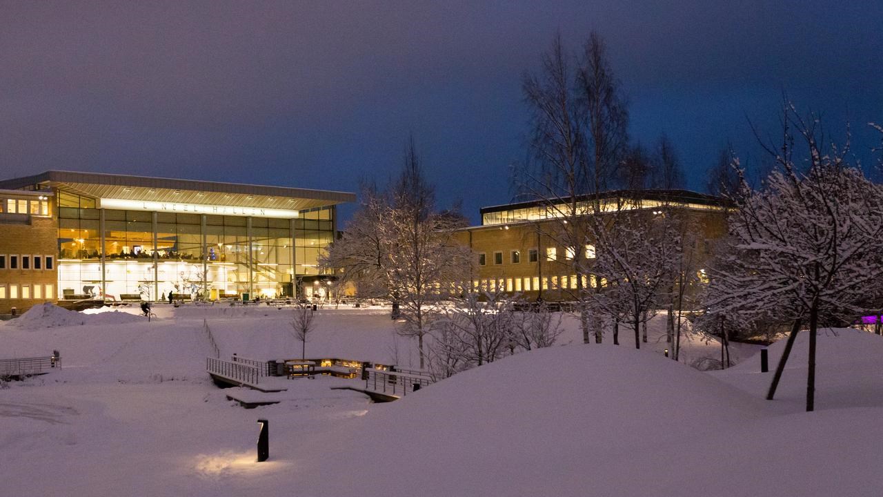 Vy över snötäckt Campus Umeå i skymningen i december.
