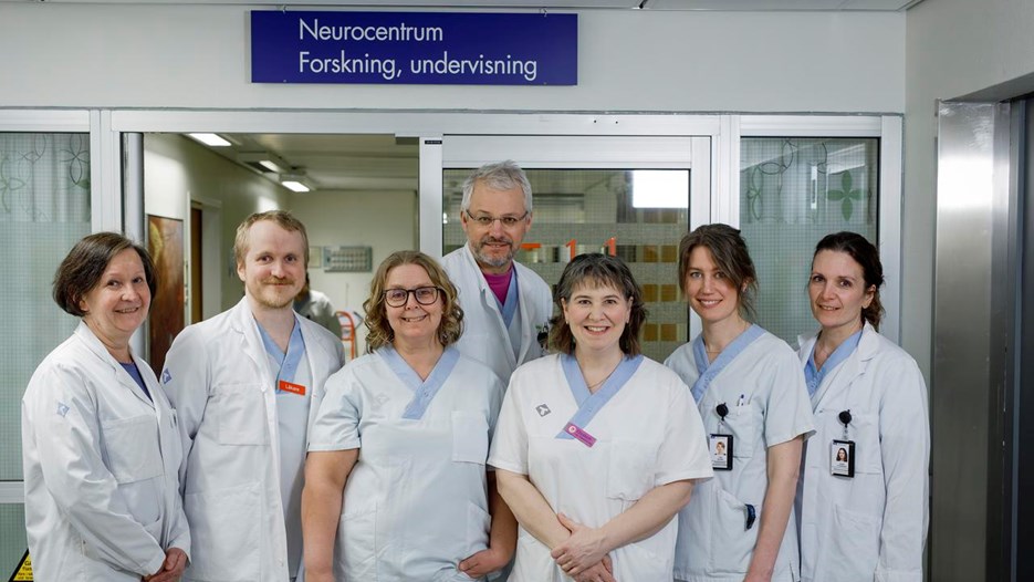 Gruppbild på Lena Bylund, doktoranden Ivar Winroth, Nina Sundqvist, professor Peter Andersen, Elisabeth Müller Granberg, Tina Björn och forskaren Karin Forsberg som står utanför Neurologens forskningsavdelning och tittar in i kameran. På en skylt ovanför dörren står Neurocentrum Forskning, undervisning.