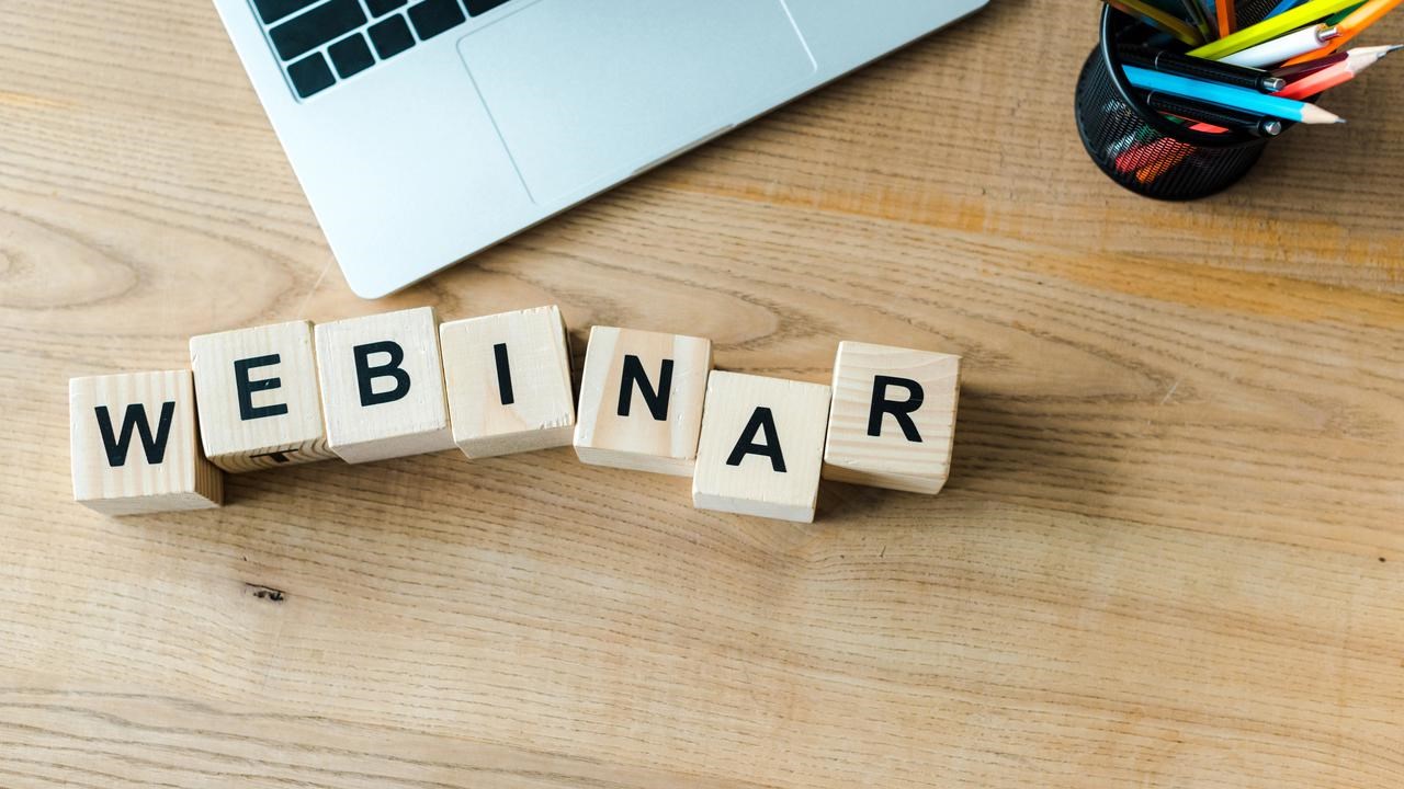Träklossar på skrivbord bredvid laptop som bildar ordet webinar.