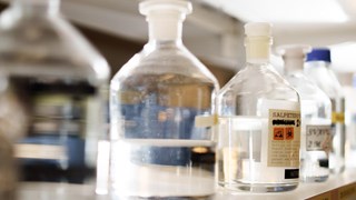 Bild på glasflaskor med kemiska vätskor på en hylla.