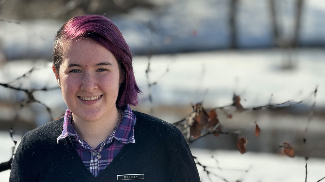 Hanna står vid universitetsdammen. Hen har lila hår, kammat med en sidbena.