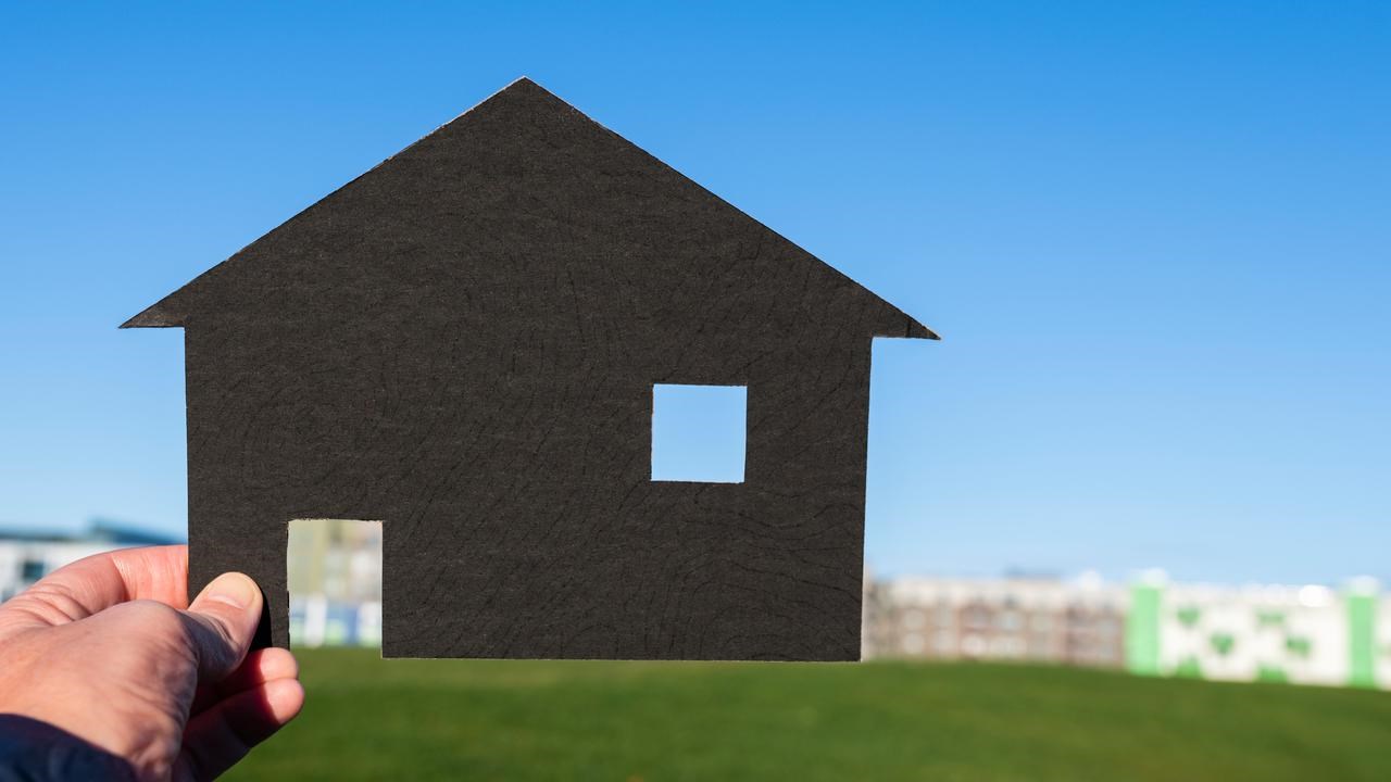 Hand som håller upp schablon av ett hus mot en kulle.