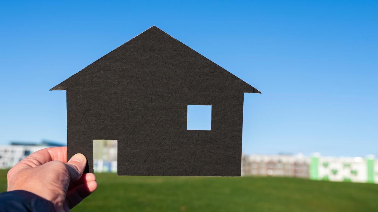 Hand som håller upp schablon av ett hus mot en kulle.