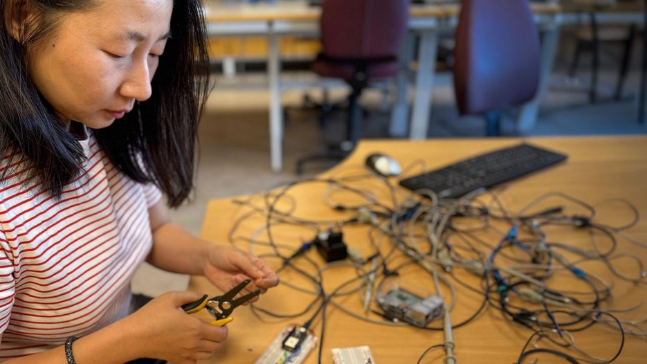 En kvinna som sitter vid ett bord och arbetar med elektronik.