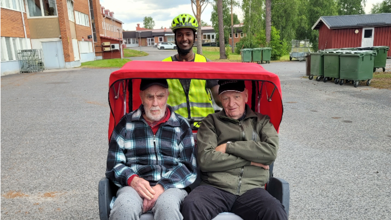 Två äldre män blir skjutsade på elcykel av leende ung man.
