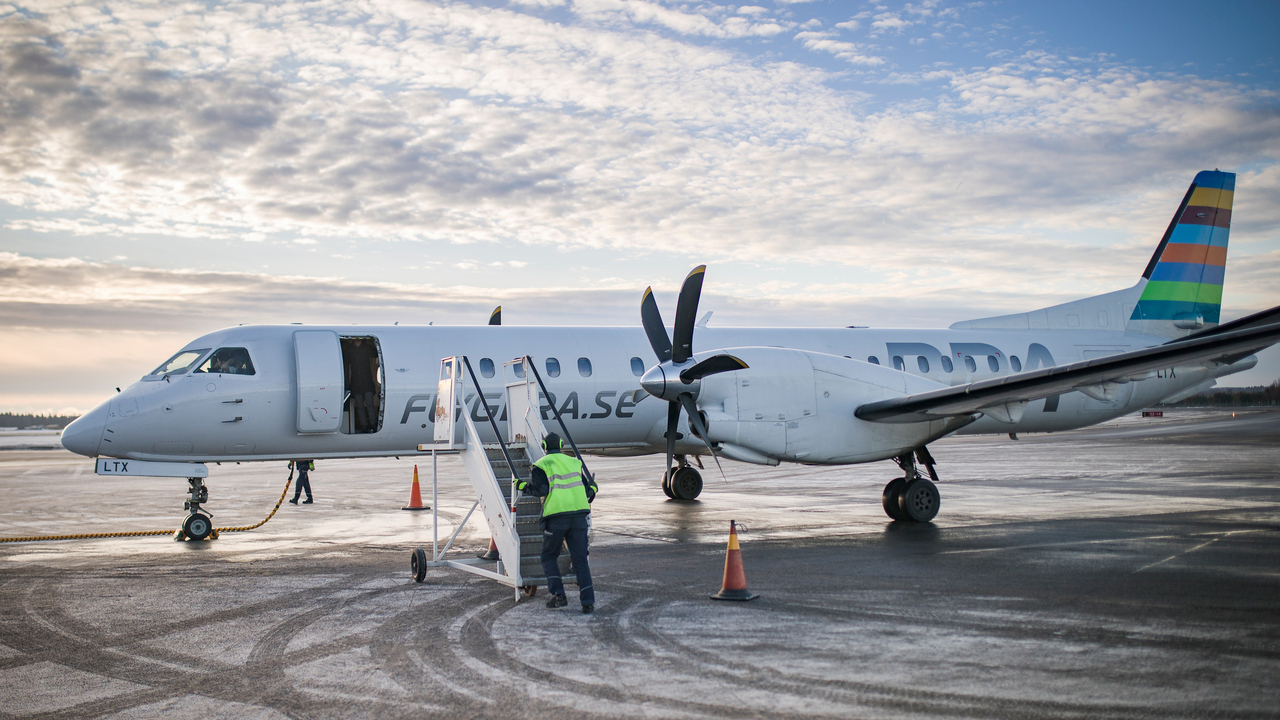 Ett flygplan som st&aring;r p&aring; landningsplattan p&aring; Ume&aring; flygplats. En flygplatsanst&auml;lld h&aring;ller p&aring; att ansluta trappan f&ouml;r att passagerare ska kunna g&aring; ur planet.