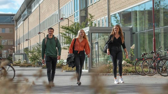 Three students are walking along the Social Sciences Building on Campus Umeå.