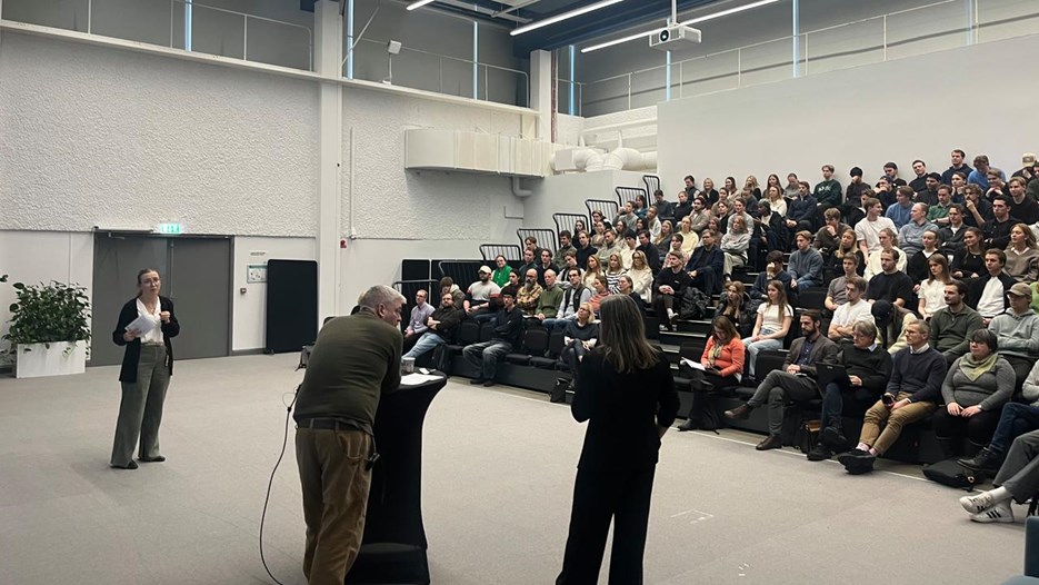 Three people are standing in front of a sitting audience an big room.