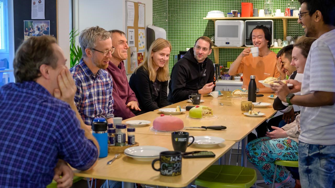 A group of people sitting around a wooden table sharing cake and talking