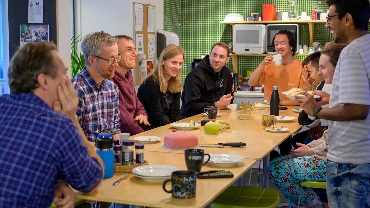 A group of people sitting around a wooden table sharing cake and talking