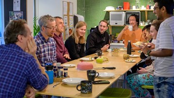 A group of people sitting around a wooden table sharing cake and talking