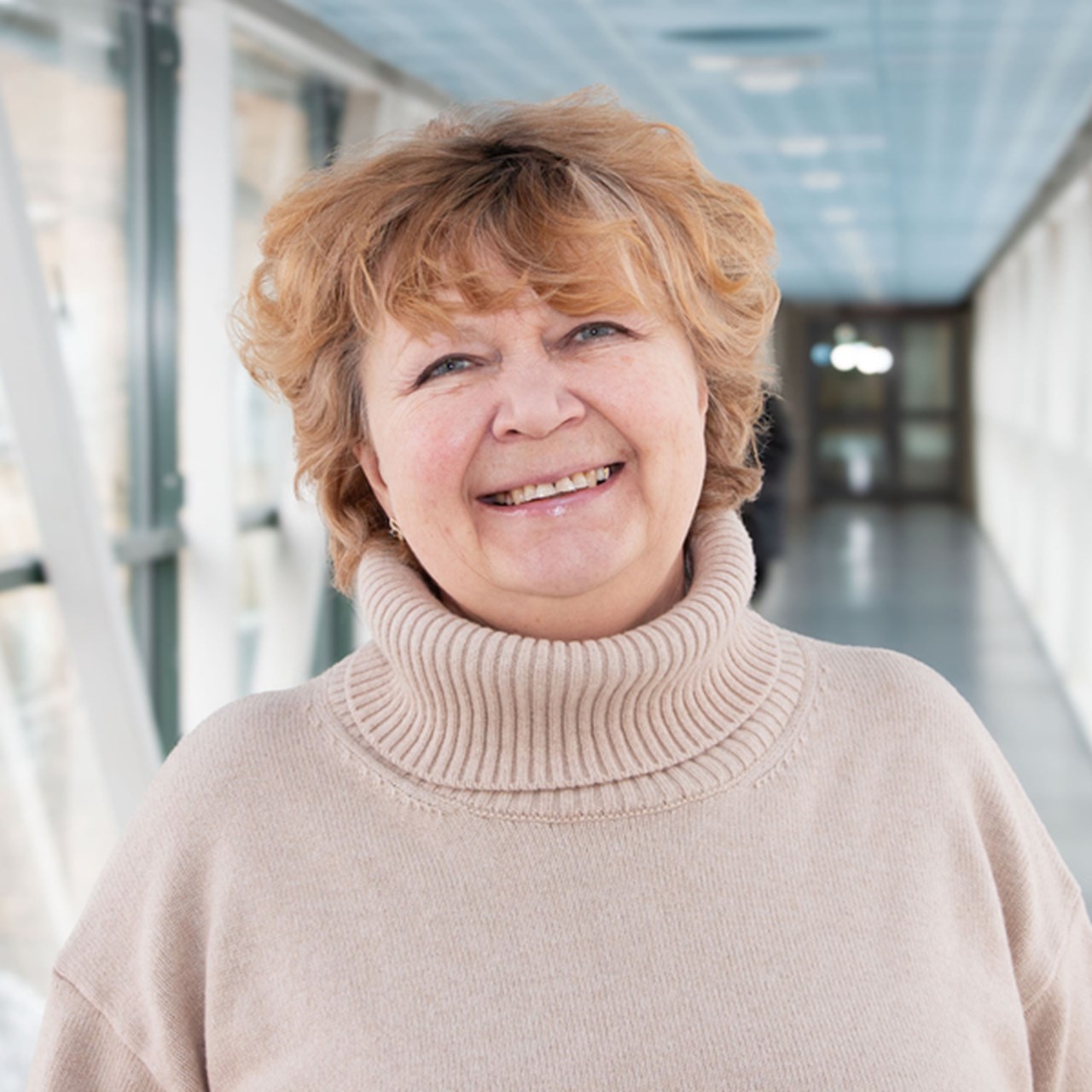 Professor Nina Khairova i en ljus korridor, iklädd en beige tröja. Hennes hår är blont och kort och hon ler.