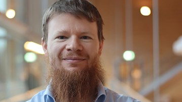 Alexandre Bartel i kort hår och skägg, står vid fönstret i ljusblå skjorta