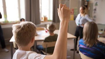 Mellanstadiebarn i klassrum. Pojke räcker upp handen.