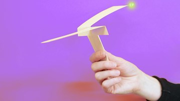 A hand holding a paper helicopter with a smal LED light attatched.