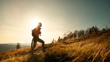 Kvinna med ryggsäck promenerar intill ett rapsfält. 