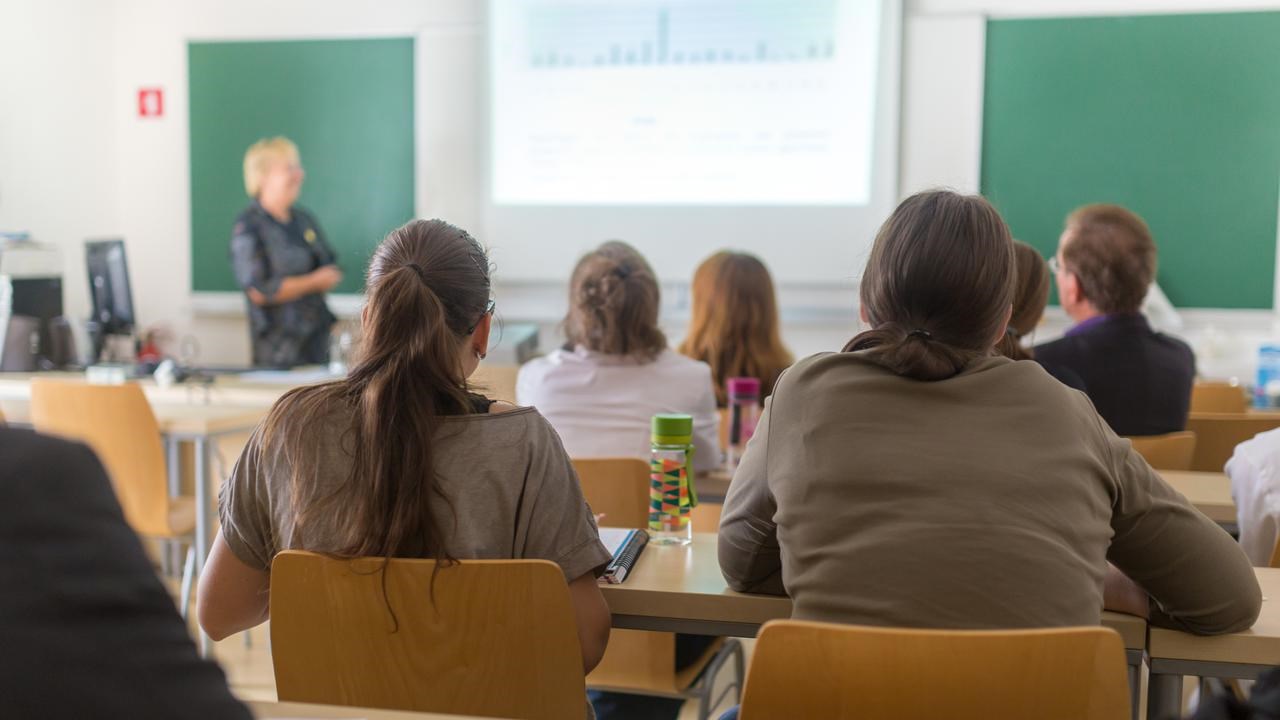 Föreläsningssal på universitet med studenter i förgrunden och en lärare vid tavlan.