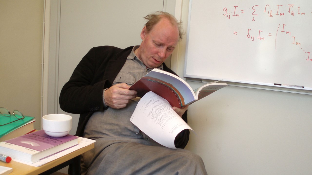 Bild av professor Roland Häggkvist som sitter på en stol och läser en tidsskrift