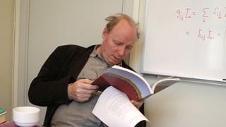 Bild av professor Roland Häggkvist som sitter på en stol och läser en tidsskrift 