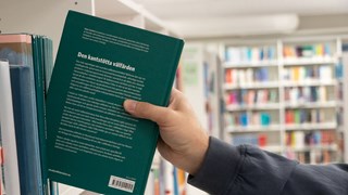 En arm plockar ut en bok från en bokhylla.