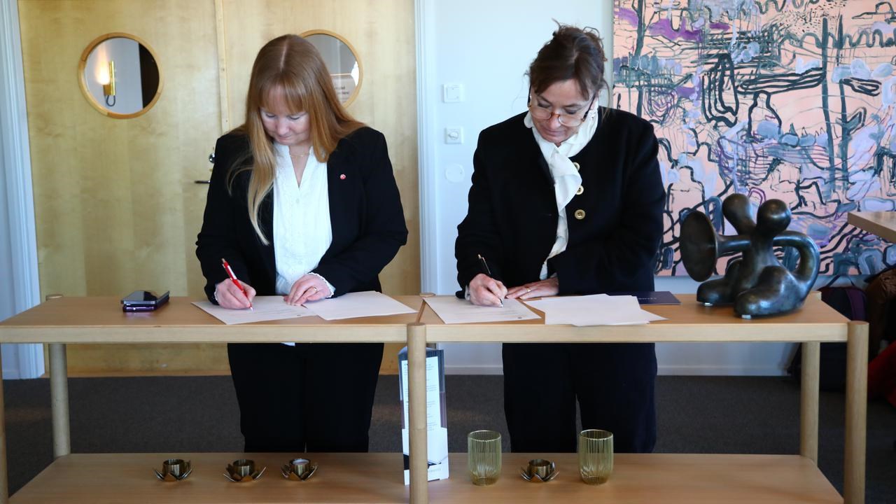 Tv&aring; kvinnor skriver p&aring; papper vid ett skrivbord.