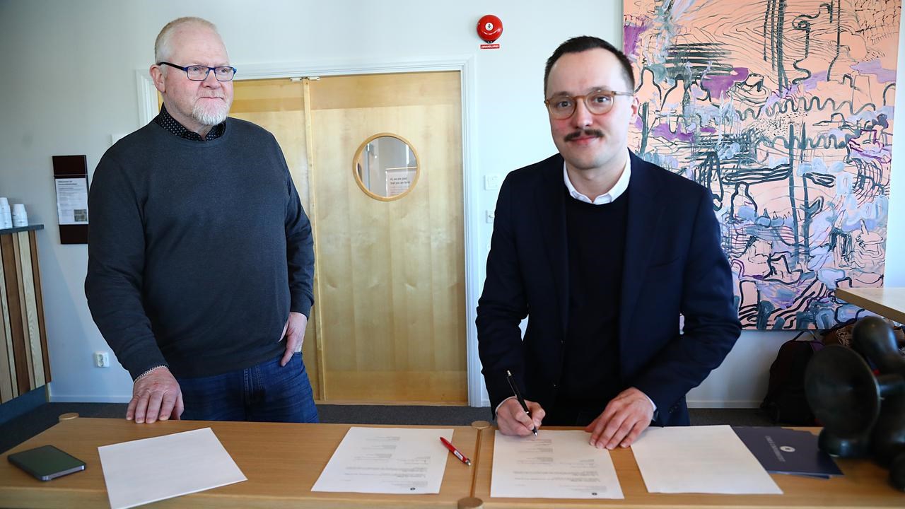 Tv&aring; m&auml;n som st&aring;r bakom ett bord med papper p&aring;.