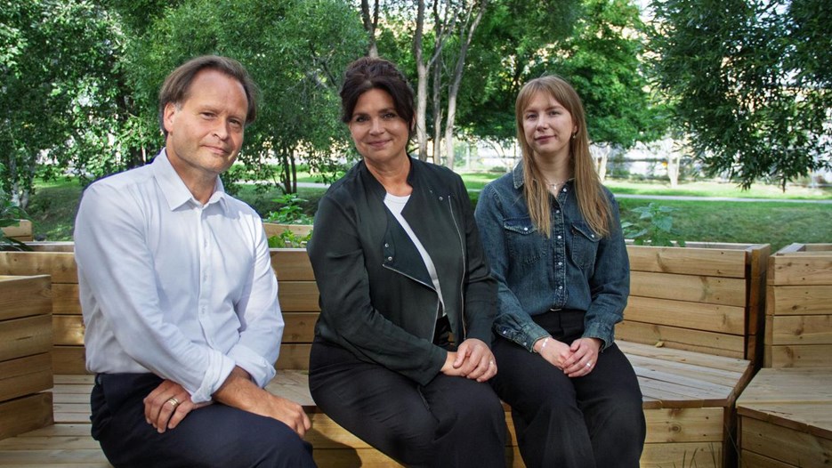 Tre personer som sitter på en bänk i en park.
