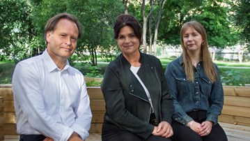 Tre personer som sitter på en bänk i en park.