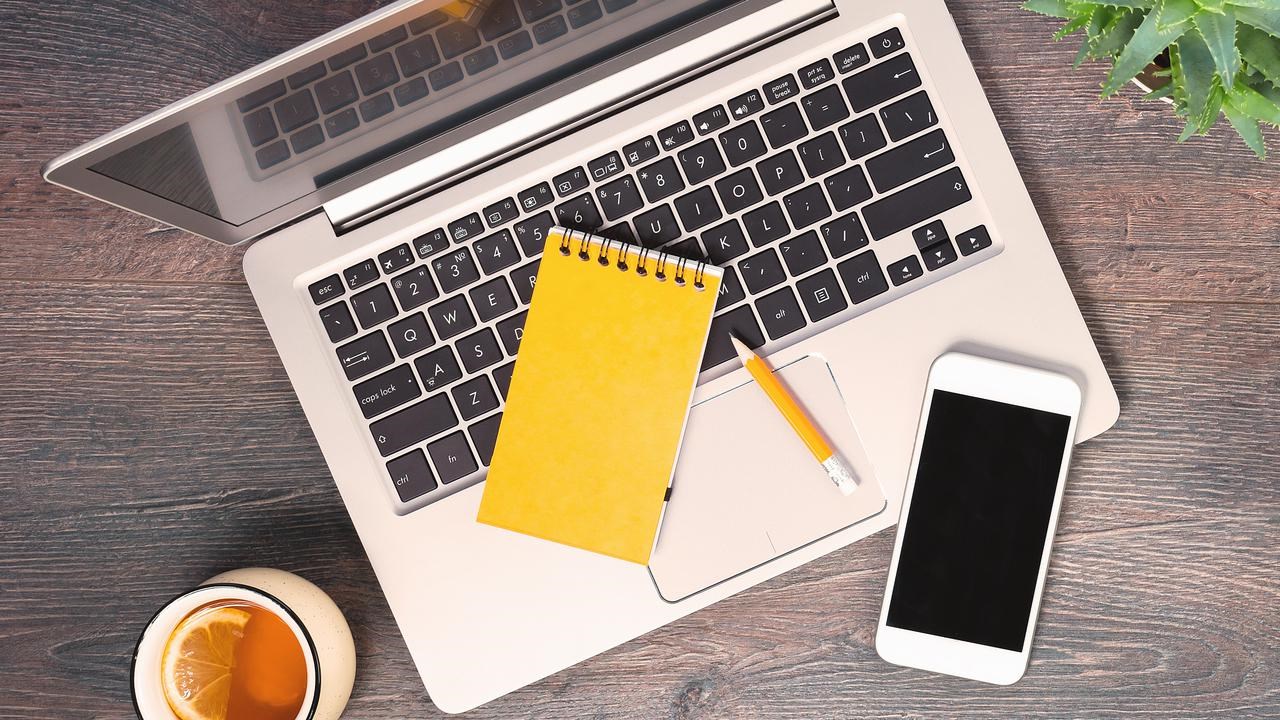 Dator, anteckningsblock, mobil och penna fotat uppifrån på ett bord.