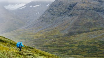 En person med en blå ryggsäck som går nedför ett fjäll.