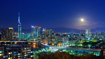 A view of a city at night with a full moon.