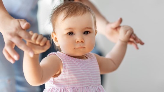 Liten flicka lär sig gå med hjälp av sin mamma.